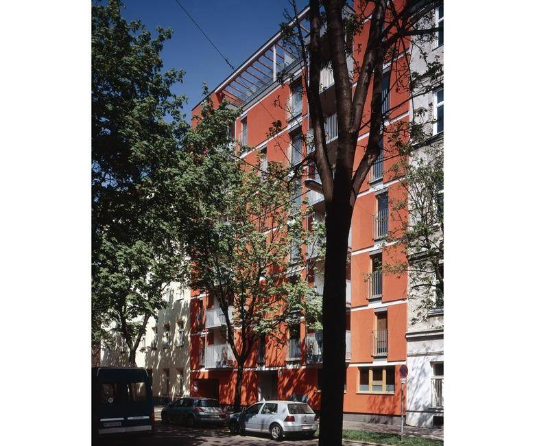 Auffälliges Wohngebäude mit leuchtend orangeroter Fassade und vielen grünen Bäumen davor.