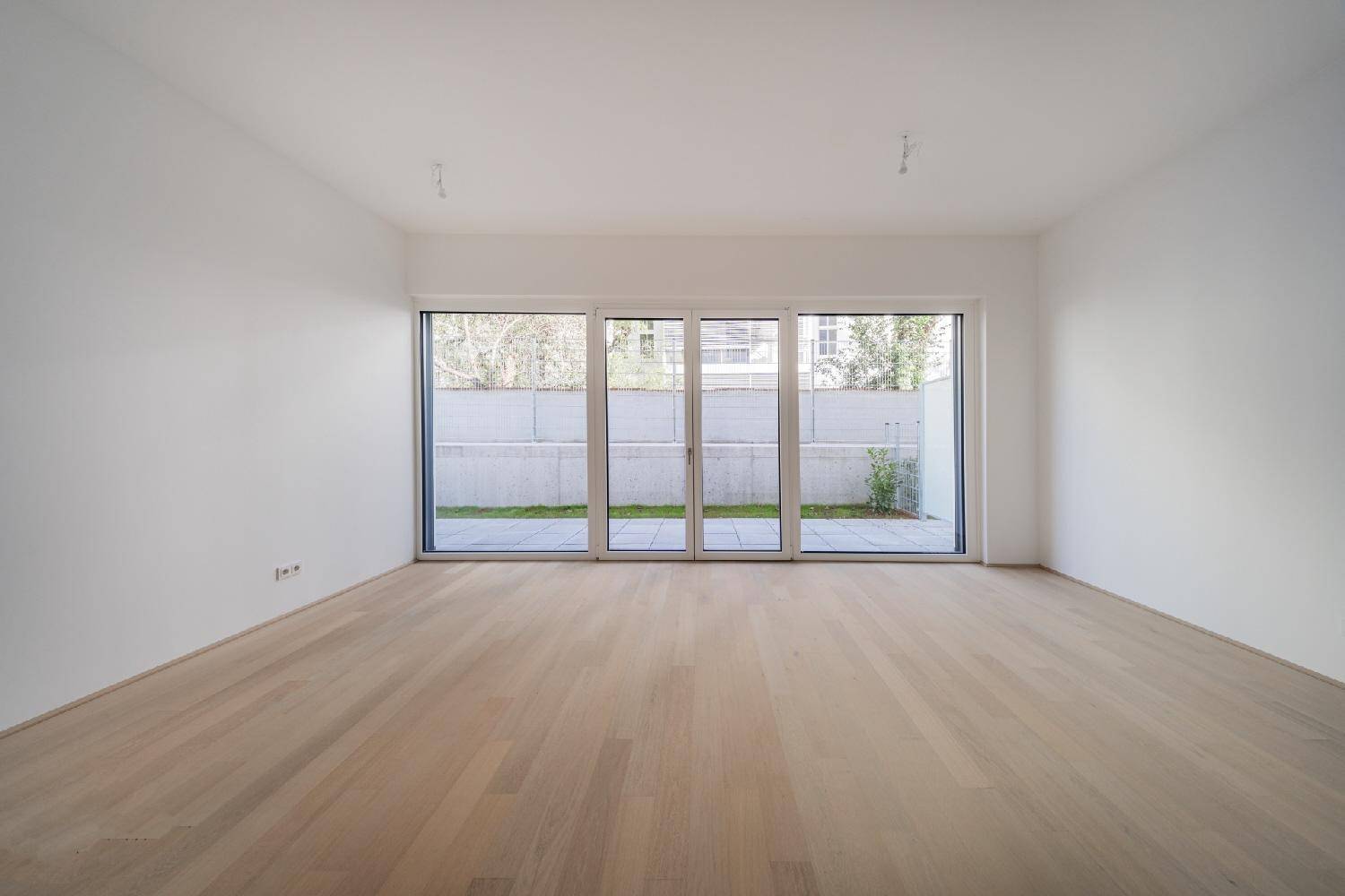 Heller, leerer Raum mit großen Fenstern und Zugang zur Terrasse oder zum Garten.