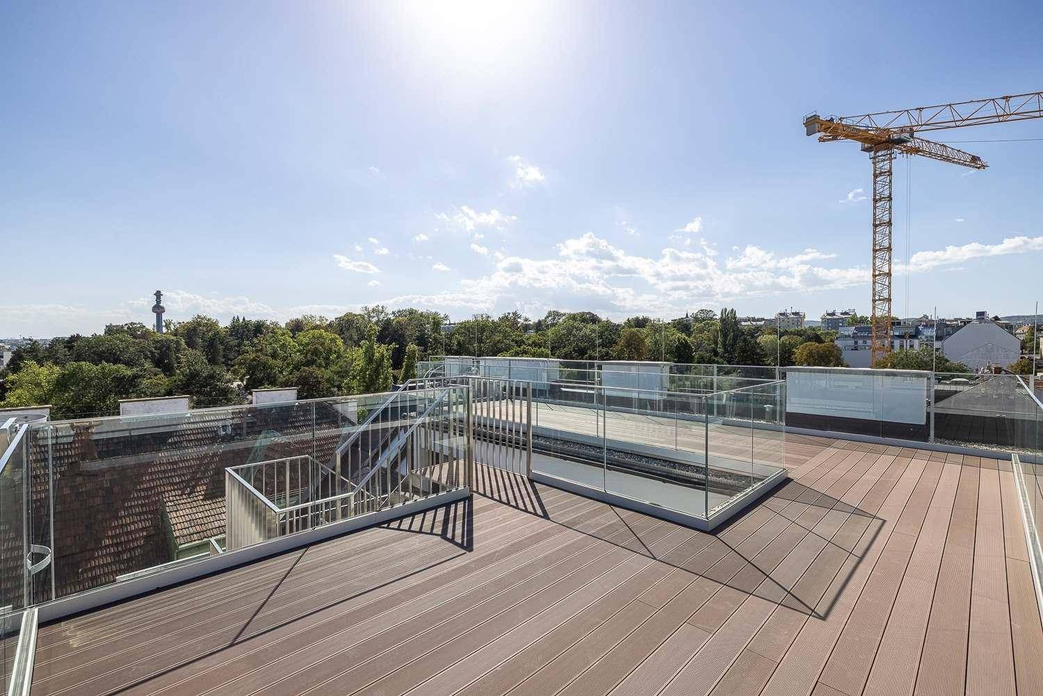 Weitläufige Dachterrasse mit Holzbelag und Glasgeländer, bietet einen sonnigen Außenbereich.