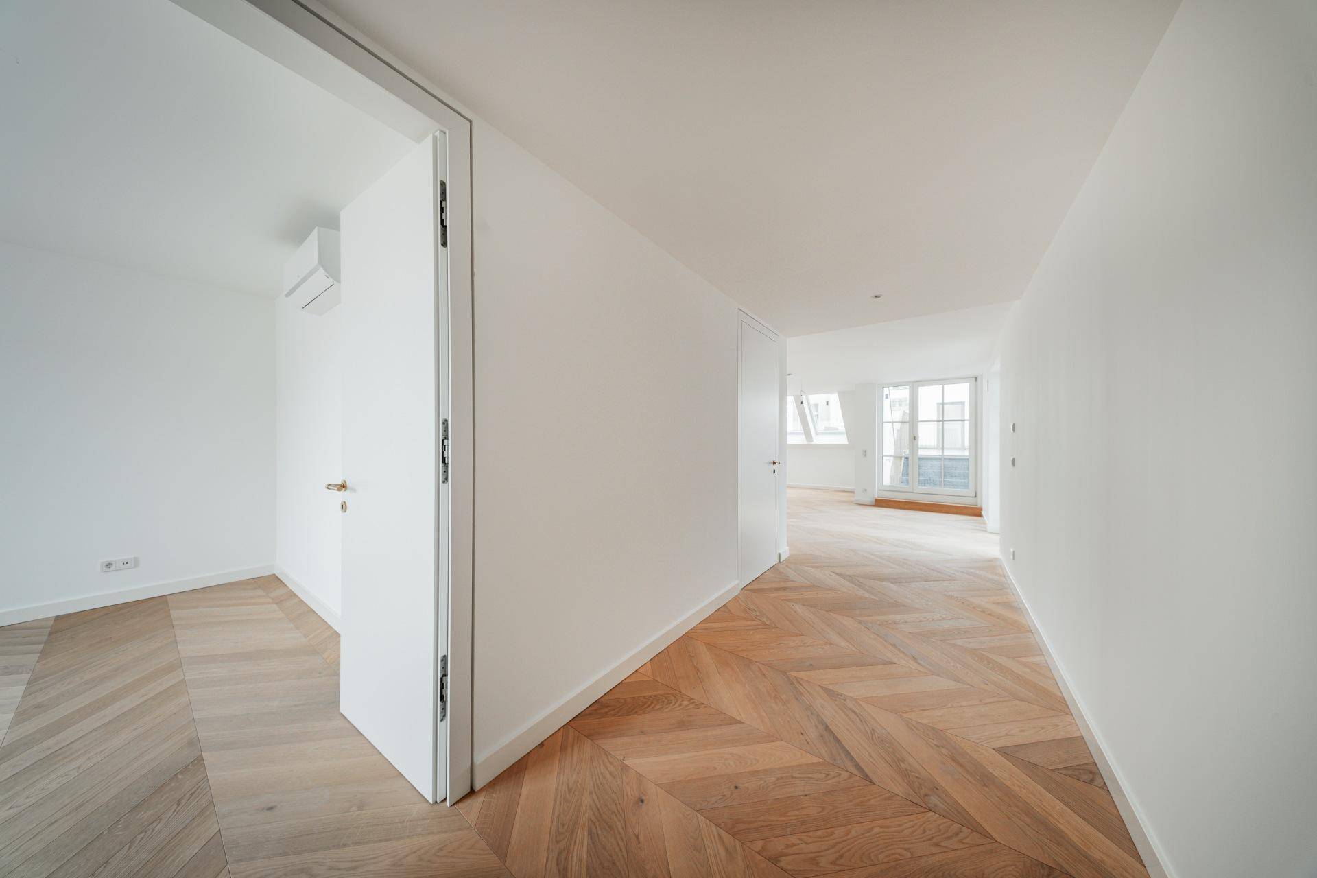 Heller Flur mit Fischgrätparkett, der zu weiteren Zimmern und einem Balkon führt.