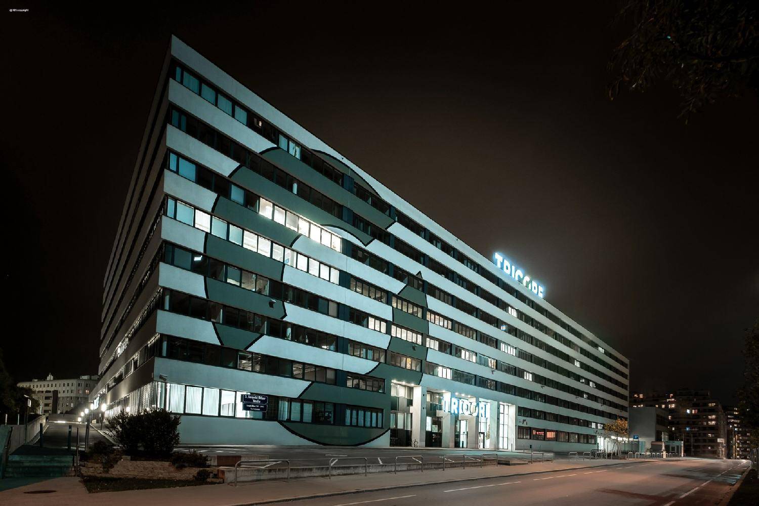 Modernes Bürogebäude bei Nacht, beleuchtet mit großen Fenstern und einer markanten Fassadengestaltung.