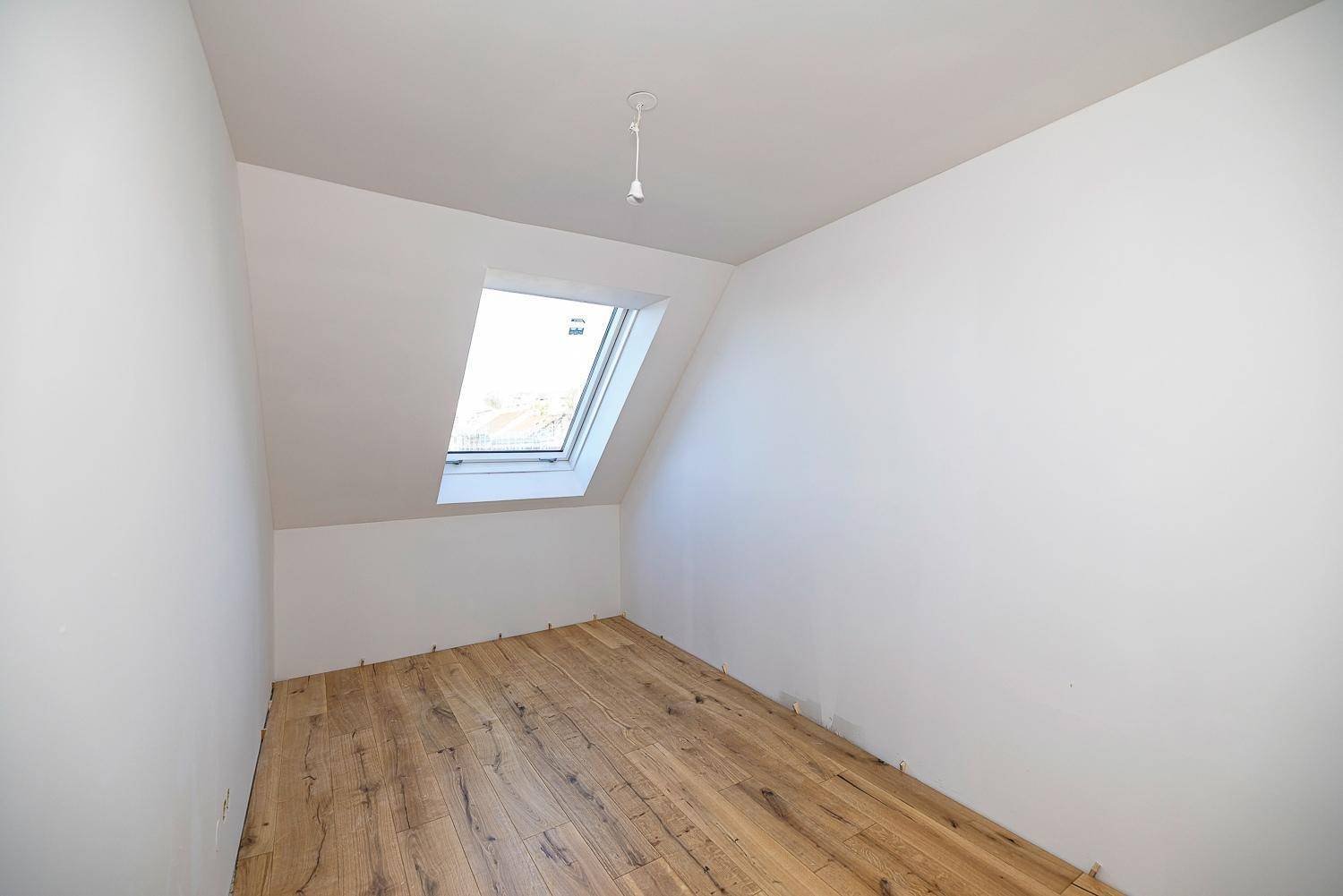 Kleiner, heller Raum im Dachgeschoss mit Holzboden und einem einzelnen Dachfenster.