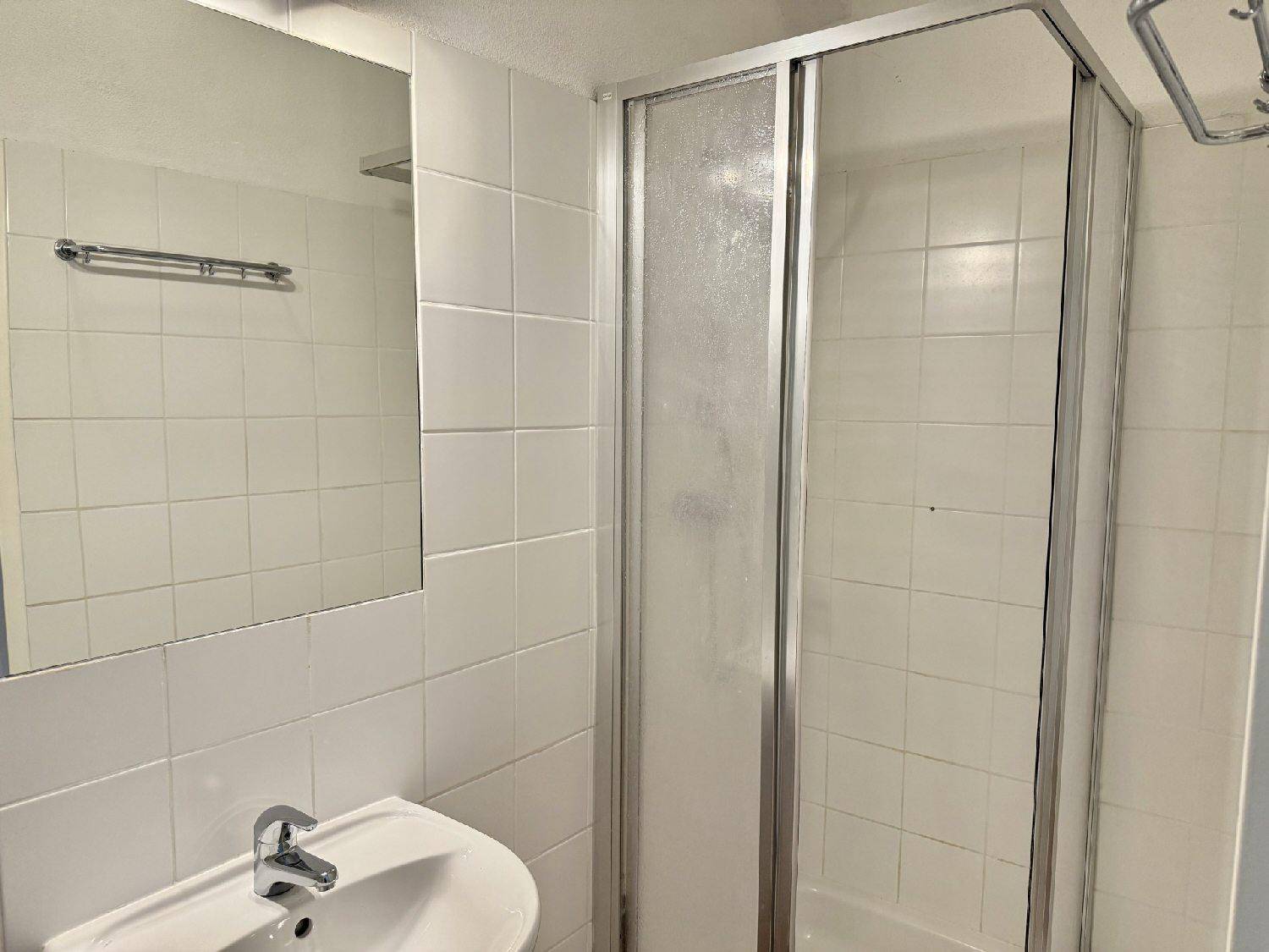 Funktionales Badezimmer mit weiß gefliesten Wänden, Waschbecken und Duschkabine.
