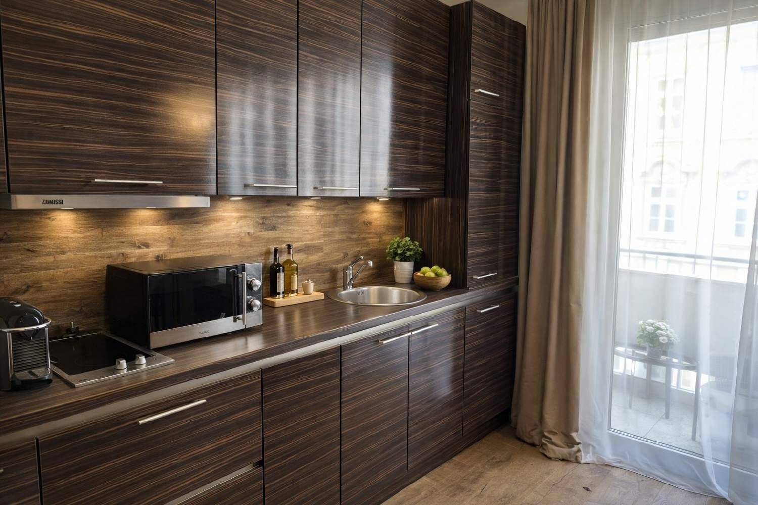 Moderne Küchenzeile mit dunklen Holzfronten, integrierten Geräten und Zugang zum Balkon.