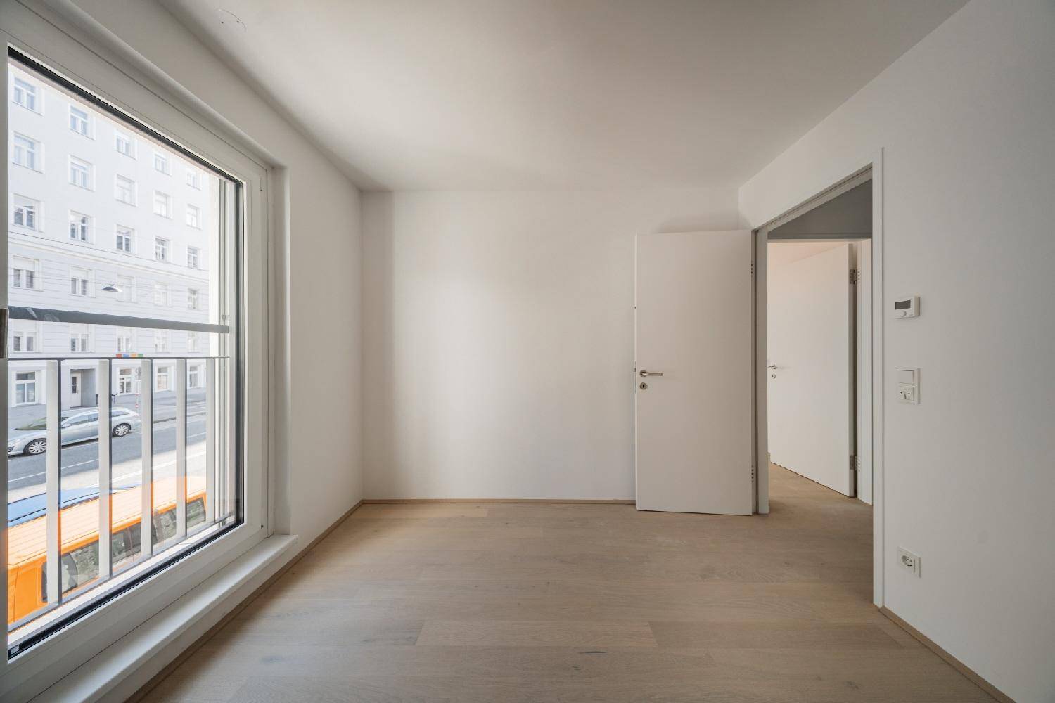 Helles Schlafzimmer mit Holzboden, großem Fenster und französischem Balkon, bietet Zugang zu weiteren Räumen.