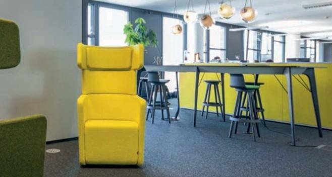 Farbenfroher, moderner Bürobereich mit gelben Sesseln, hohen Hockern und einer Pflanze, ideal für informelle Treffen oder Pausen.