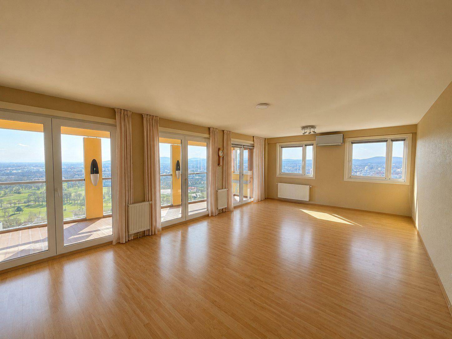 Helles Wohnzimmer mit Parkettboden, großen Fenstern und Zugang zu einem Balkon mit Weitblick.