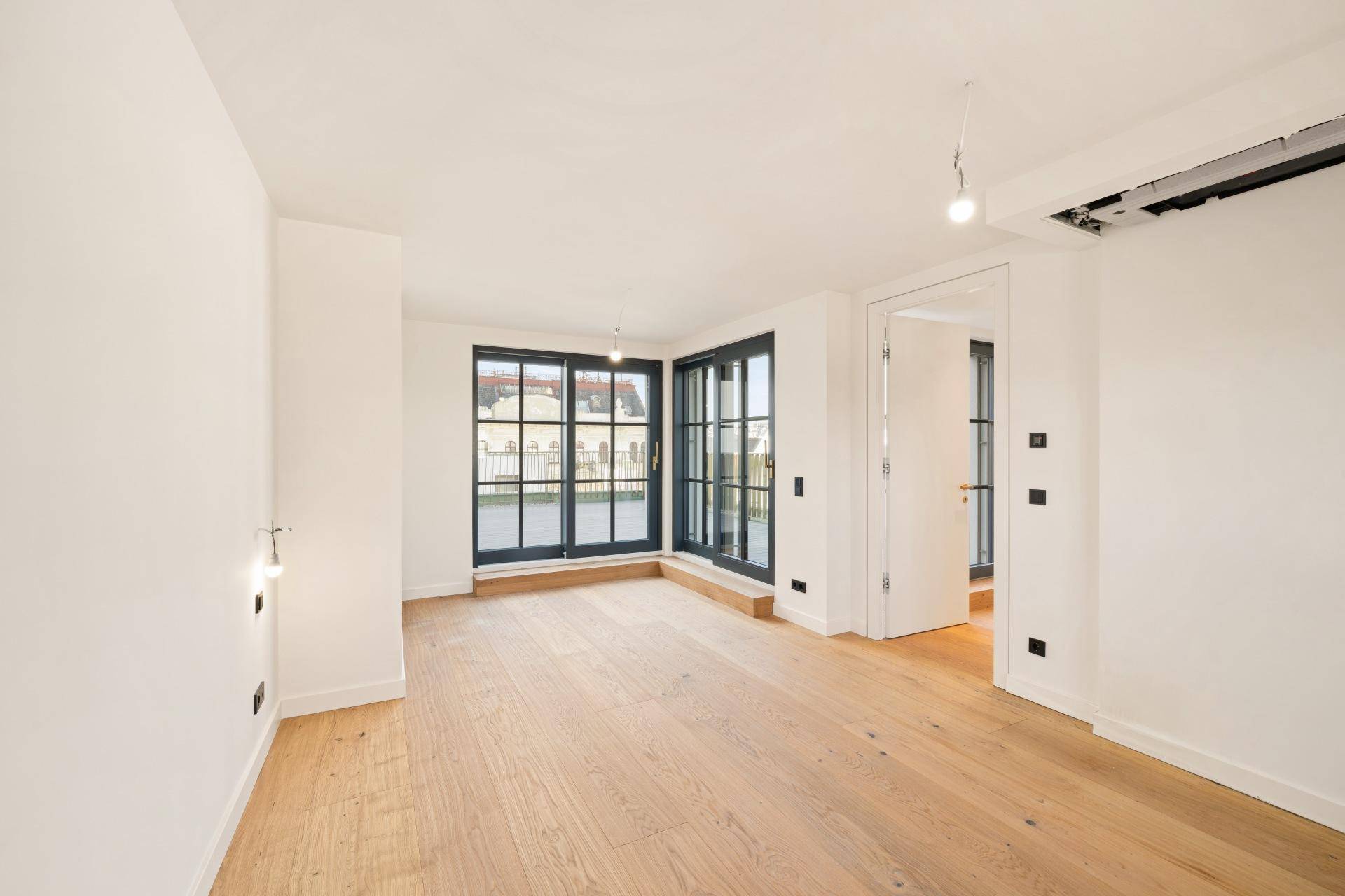 Heller Wohnraum mit Holzboden und großen Fenstertüren, die zu einem Außenbereich führen.