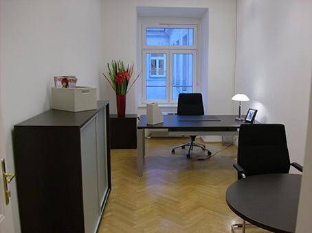 Helles Büro mit dunklem Schreibtisch, Stauraum und einem Fenster mit Blick auf einen Innenhof.