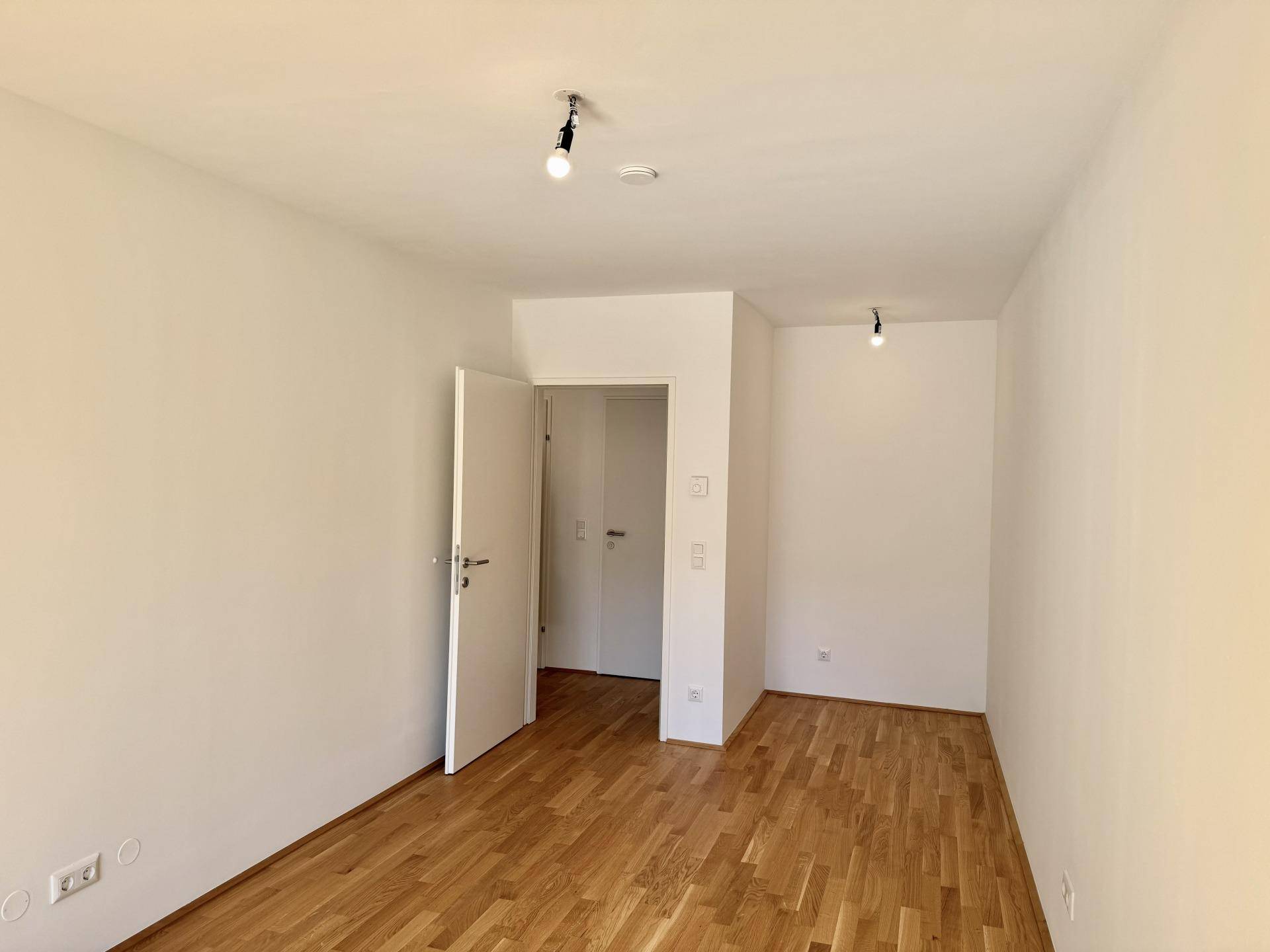 Leeres Zimmer mit Parkettboden und weiß gestrichenen Wänden, bereit für neue Bewohner.