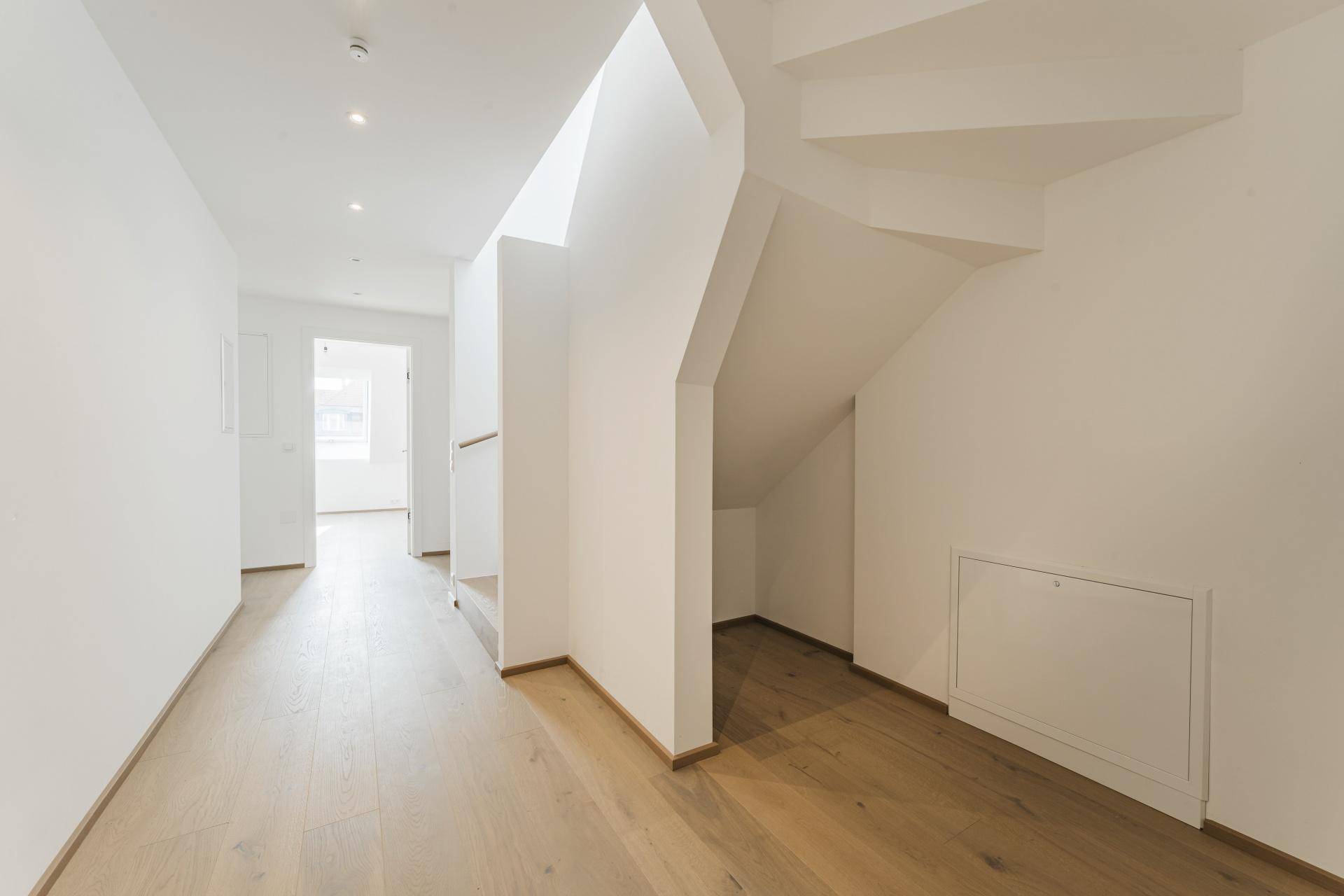 Heller Flur mit Holzboden und moderner Beleuchtung, der zu weiteren Räumen führt.
