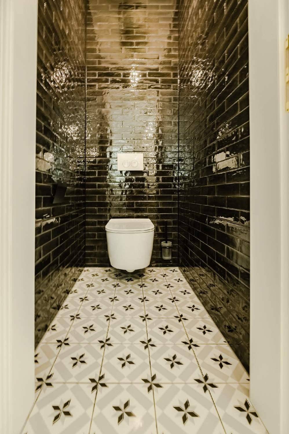 Schmale Gästetoilette mit schwarzen Hochglanzfliesen, Wand-WC und gemustertem Boden.
