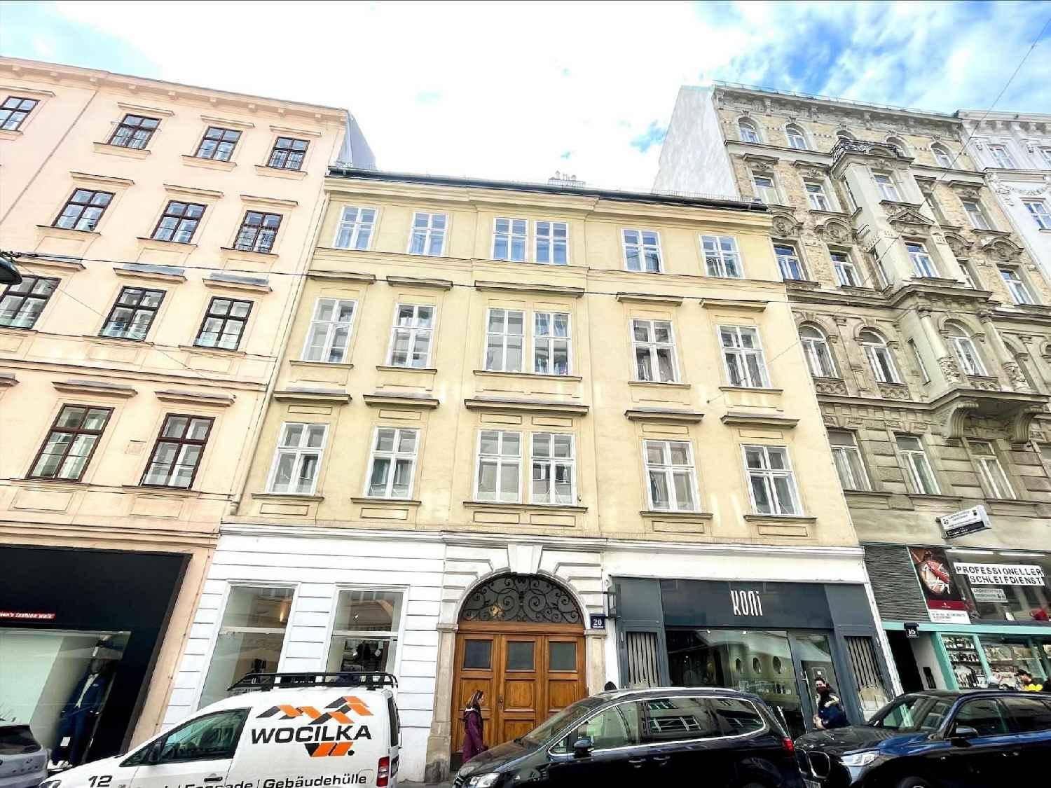 Historische Fassade eines Mehrfamilienhauses in der Stadt mit vielen Fenstern und Geschäften im Erdgeschoss.