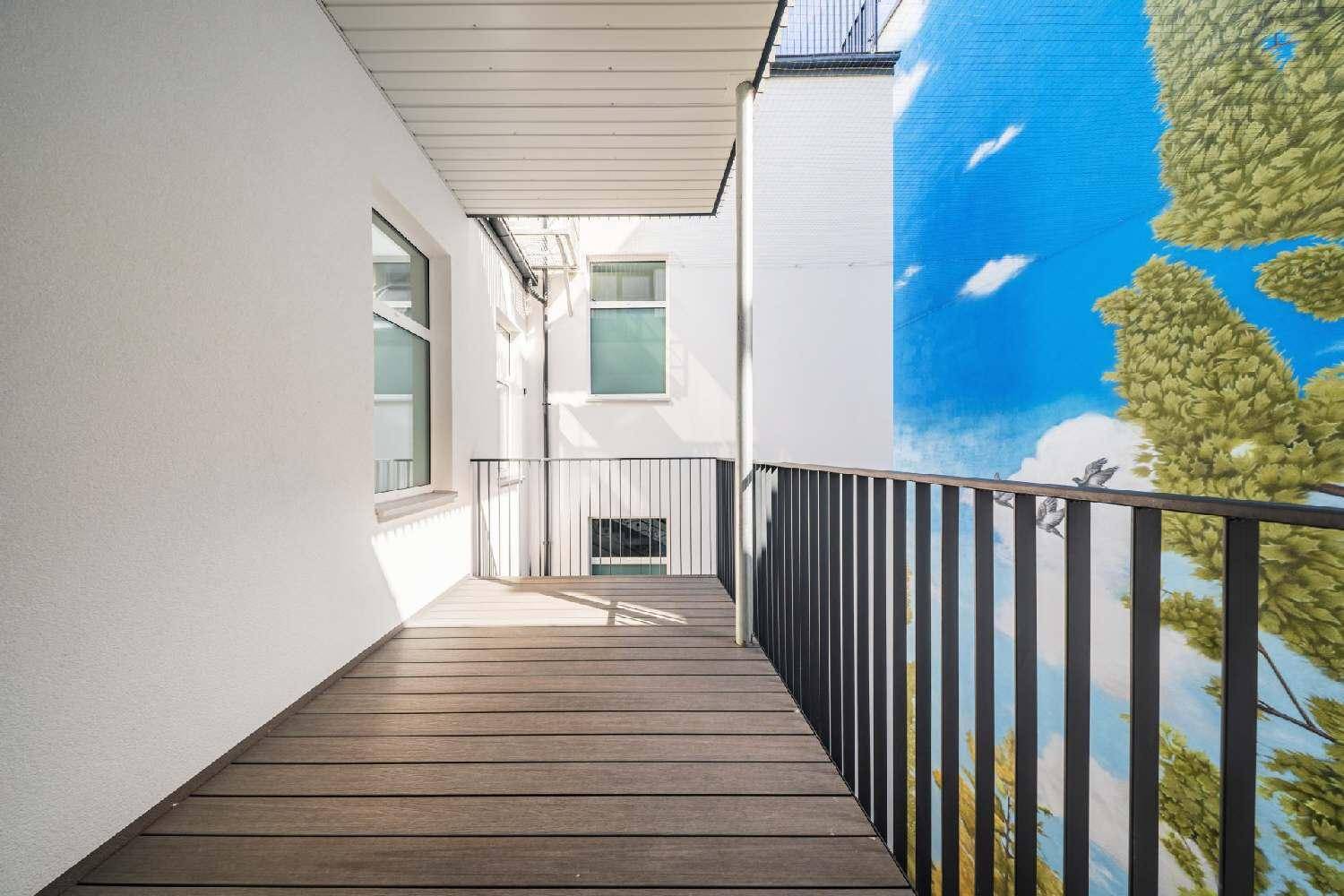 Schmaler Balkon mit Holzboden und Metallgeländer, bietet einen Blick auf eine bemalte Wand.