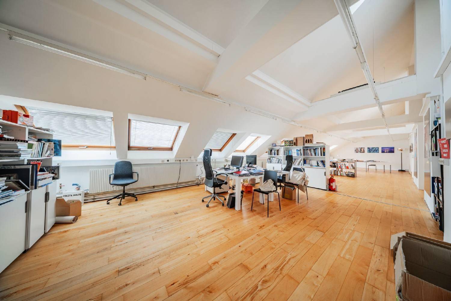 Weitläufiges Dachgeschossbüro mit Holzboden, mehreren Arbeitsplätzen und viel Tageslicht, fördert Produktivität.