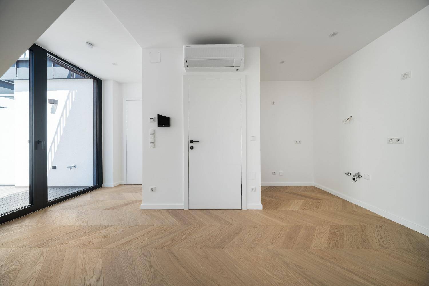 Heller Innenraum mit Klimaanlage, weißer Tür und großem Terrassenzugang mit Fischgrätparkett.