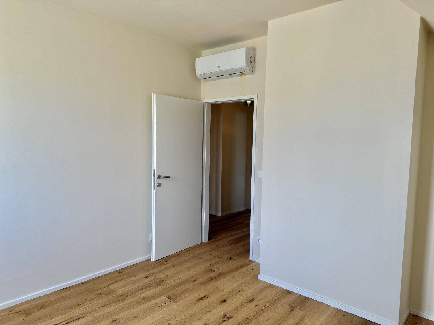 Helles Zimmer mit Holzboden, weißer Tür und installierter Klimaanlage.