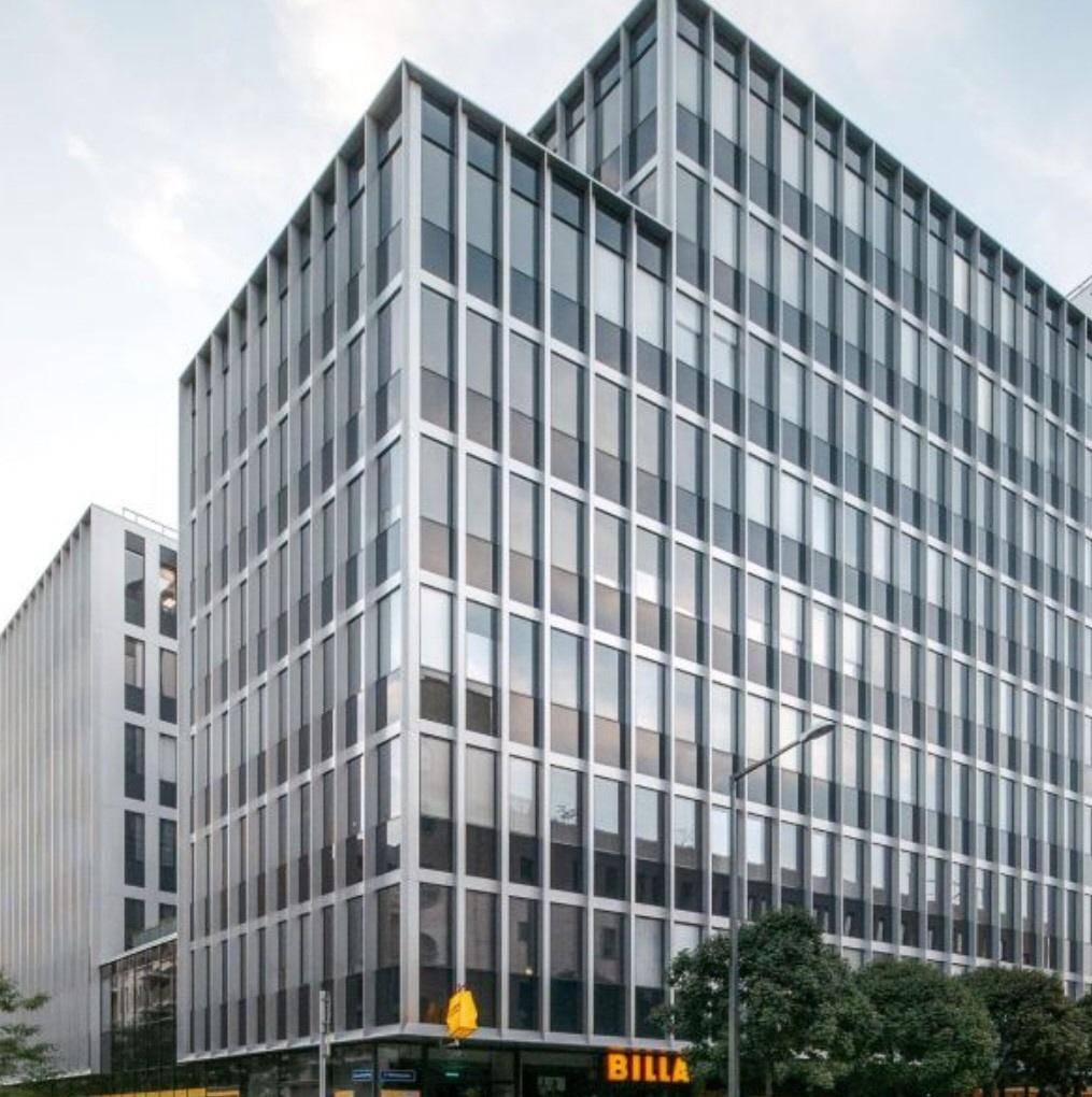 Modernes Geschäftsgebäude mit einer markanten Glas- und Metallfassade und einem Supermarkt im Erdgeschoss.
