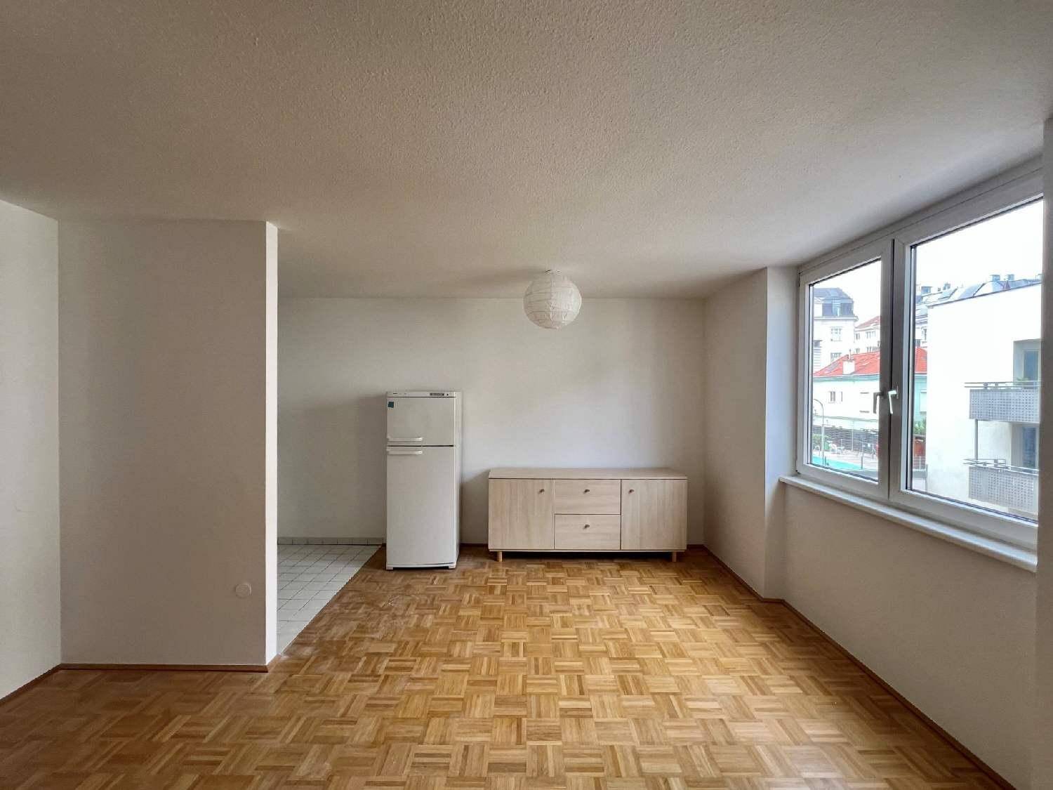 Geräumiges Zimmer mit Parkettboden, großen Fenstern und einem freistehenden Kühlschrank.