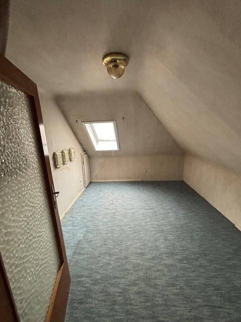 Dachzimmer mit Teppichboden, Dachfenster und ausgeprägten Dachschrägen.