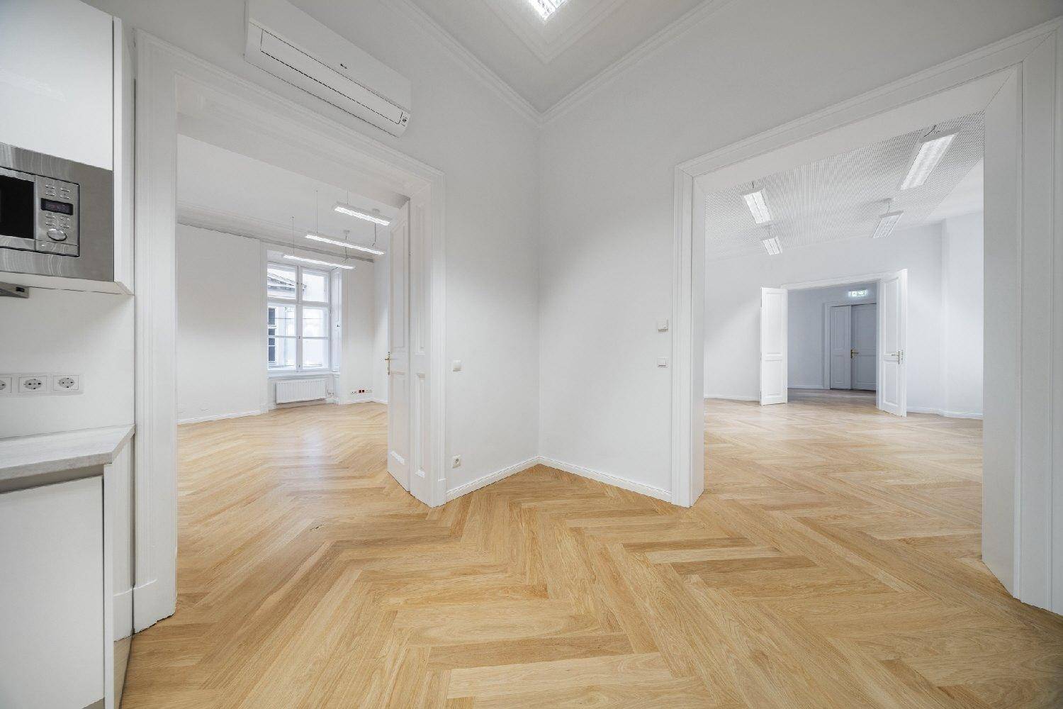 Ecke eines Raumes mit kleiner Küchenzeile, Mikrowelle und Klimaanlage, auf Fischgrätparkett.