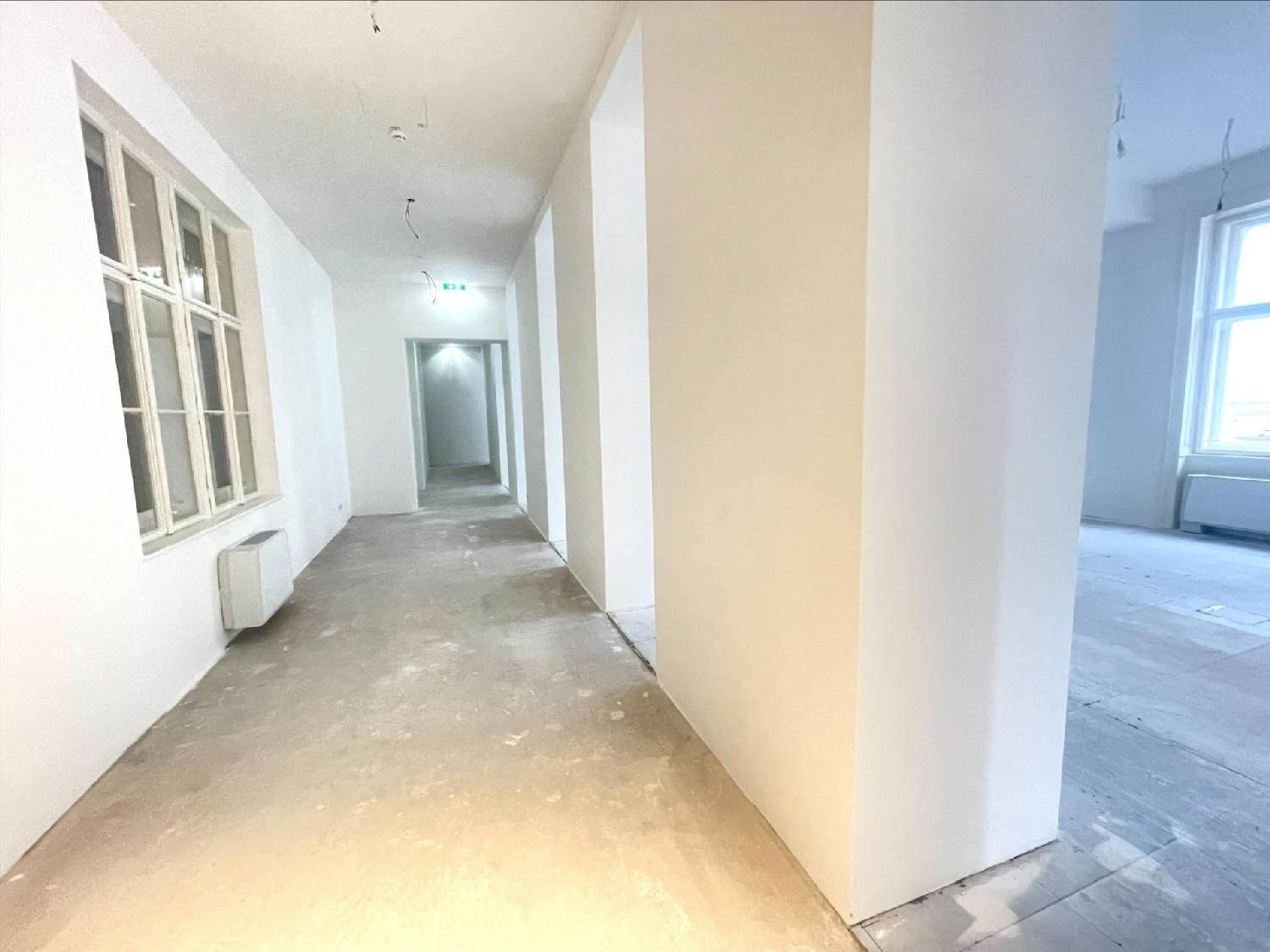 Langer, heller Flur mit hohen Decken und Betonboden, der zu weiteren Büroräumen führt.