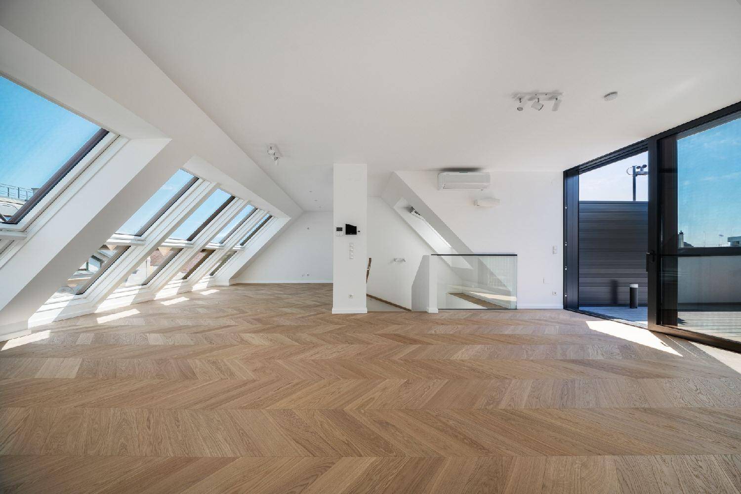 Geräumiger Wohnbereich mit Fischgrätparkett, Klimaanlage und modernem Glasgeländer zur Treppe.
