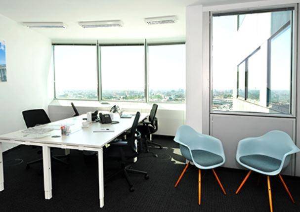 Modernes Büro mit Arbeitsplätzen und einer kleinen Sitzecke, bietet weite Aussicht durch große Fenster.