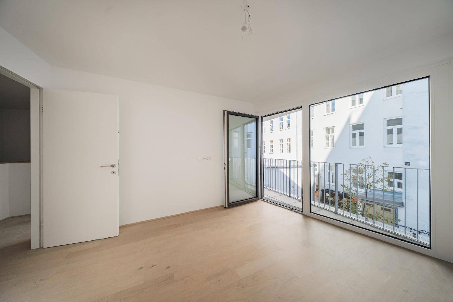 Geräumiges Schlafzimmer mit hellem Holzboden und großen Fenstern, die zu einem Balkon führen.