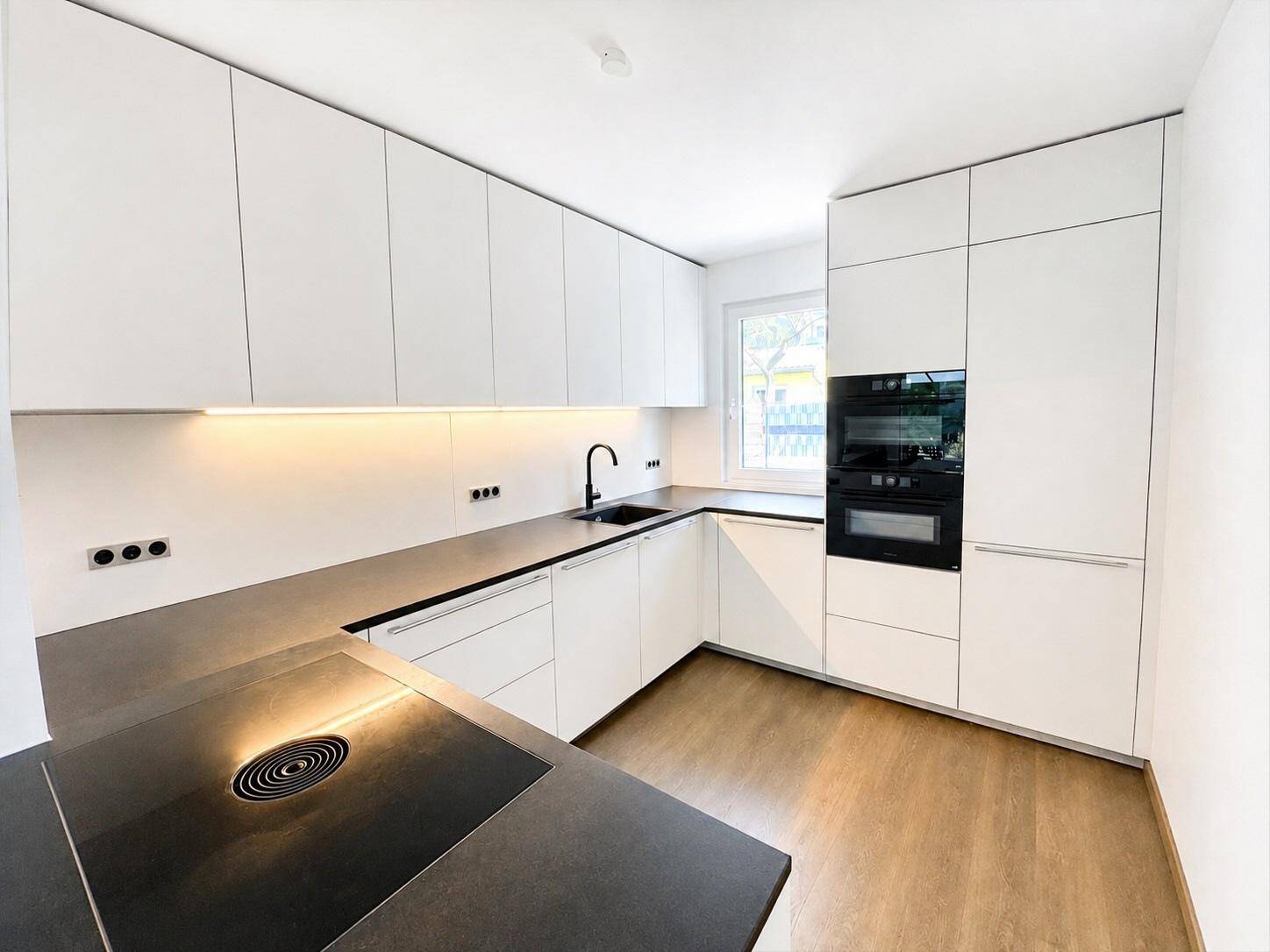 Helle, moderne Küche mit weißen Hochglanzfronten, Induktionskochfeld und integrierten Geräten.