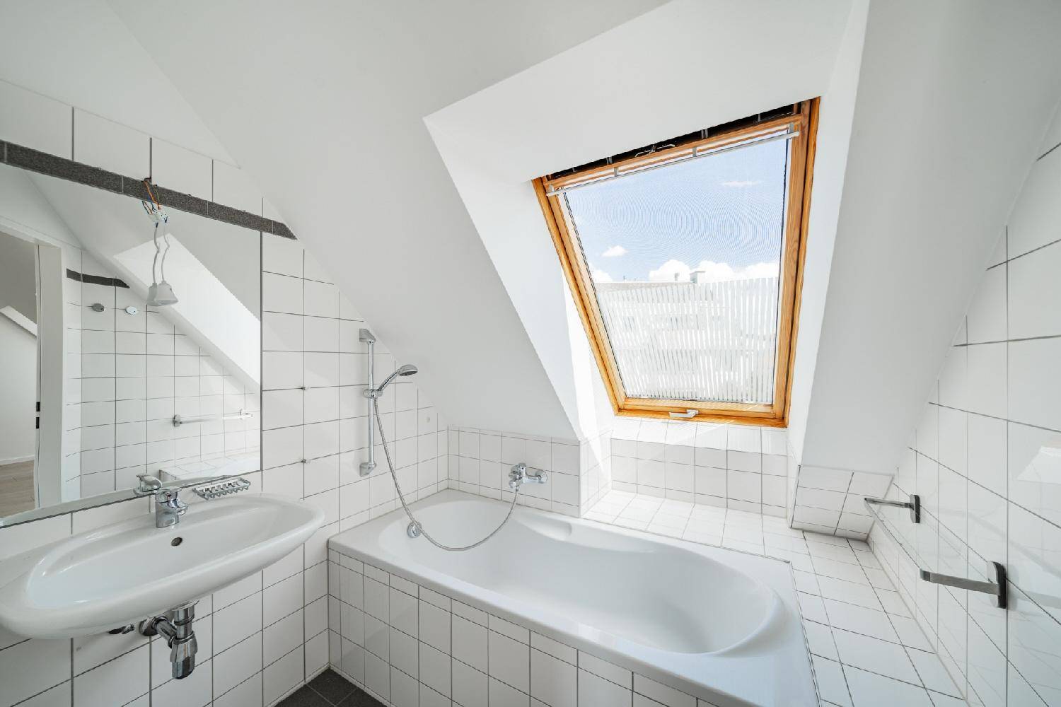 Modernes Badezimmer mit Badewanne, Waschbecken, weißen Fliesen und einem Dachfenster für natürliches Licht.