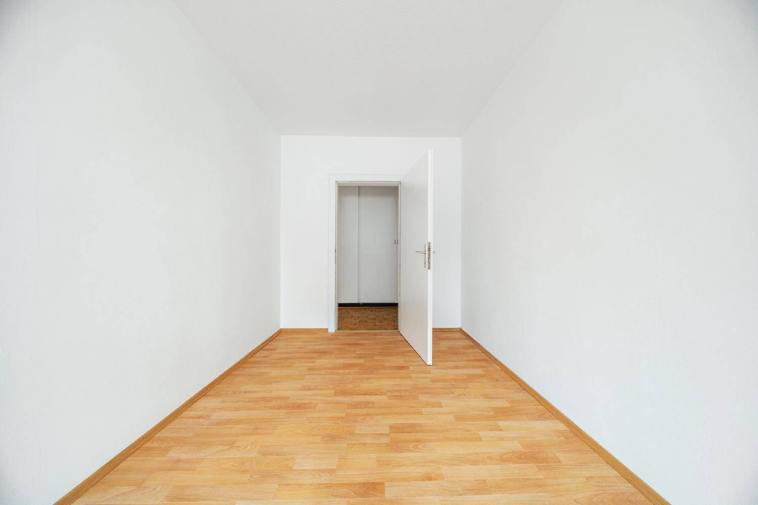 Leeres Zimmer mit Laminatboden und offener Tür, bereit für individuelle Nutzung.