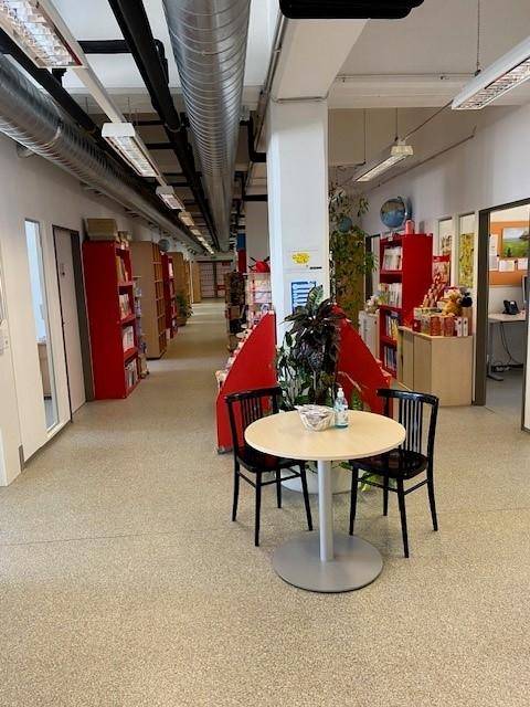 Langer Flur in einem Bürogebäude oder einer öffentlichen Einrichtung mit roten Regalen und einem kleinen Tisch.