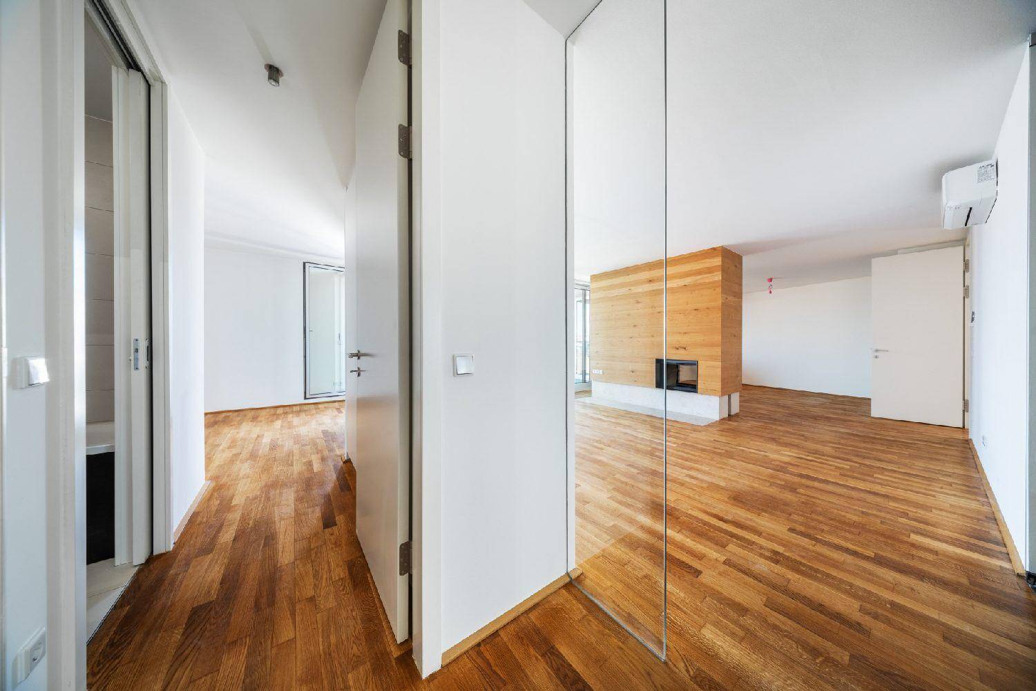 Heller Flur mit Holzboden und einer eleganten Glasabtrennung, der zu weiteren Räumen führt.