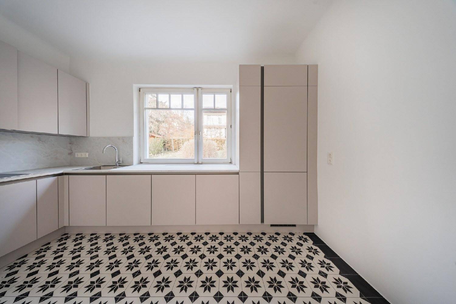 Moderne Küche mit hellen Schränken, Spüle und auffälligem schwarz-weißem Fliesenboden am Fenster.
