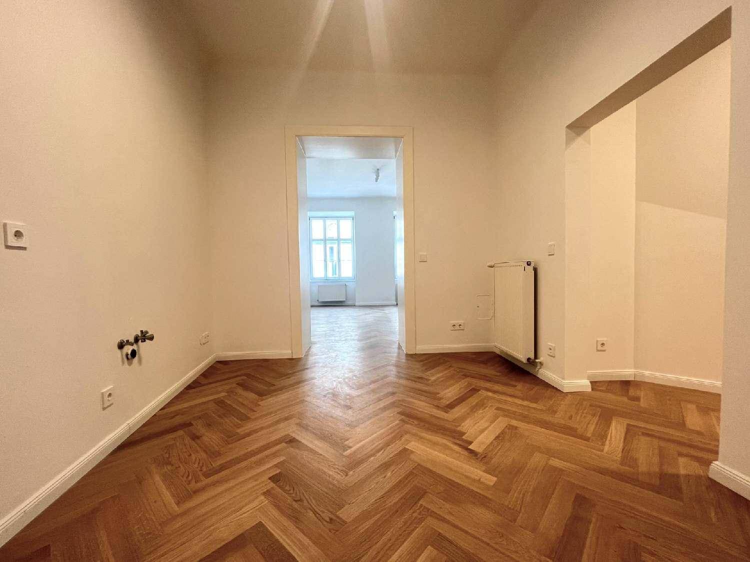 Geräumiges Zimmer mit Fischgrätparkett und Blick durch einen Durchgang in einen weiteren hellen Raum.