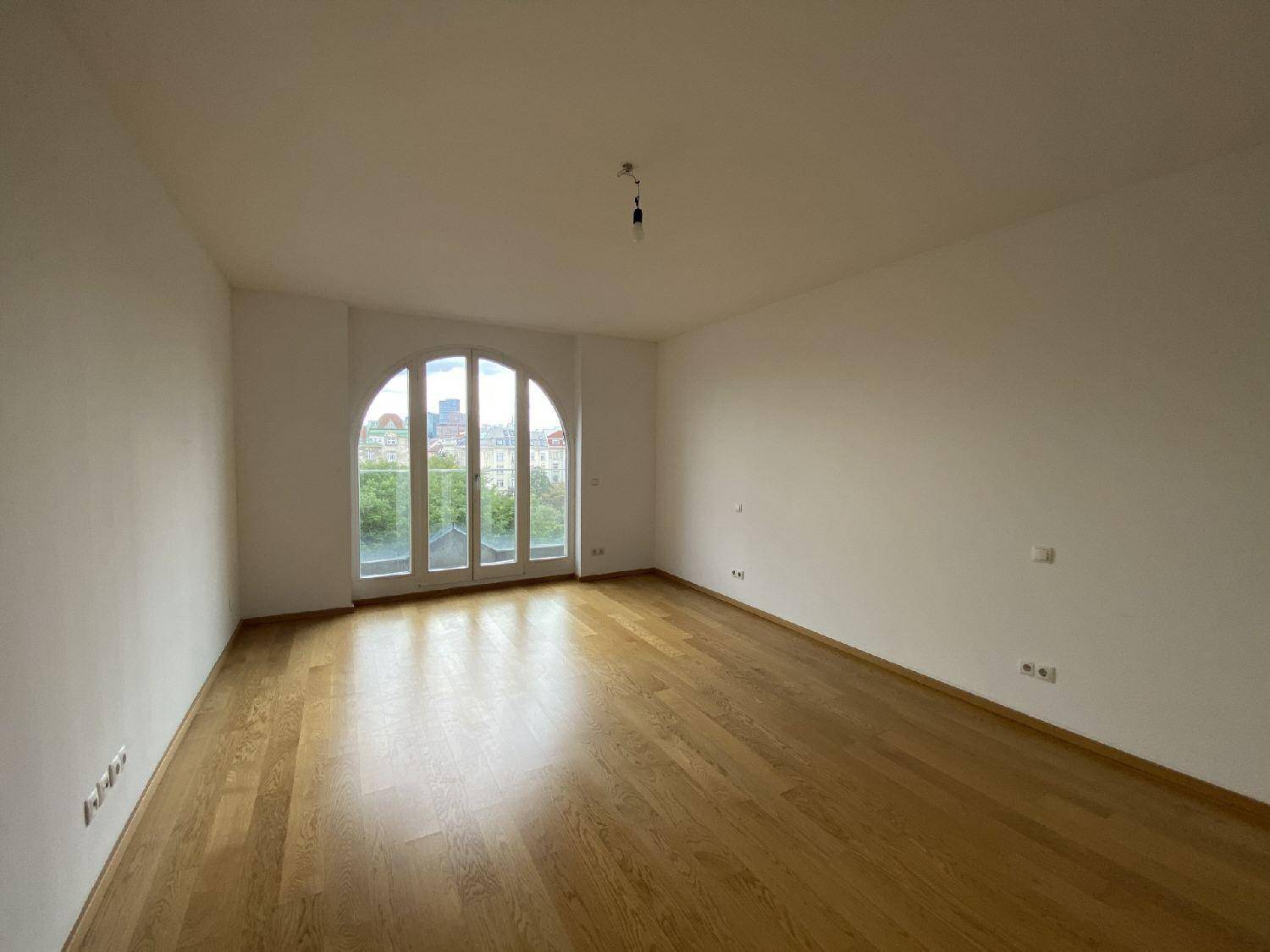 Heller Raum mit Parkettboden und einem großen Bogenfenster, das viel Tageslicht hereinlässt.