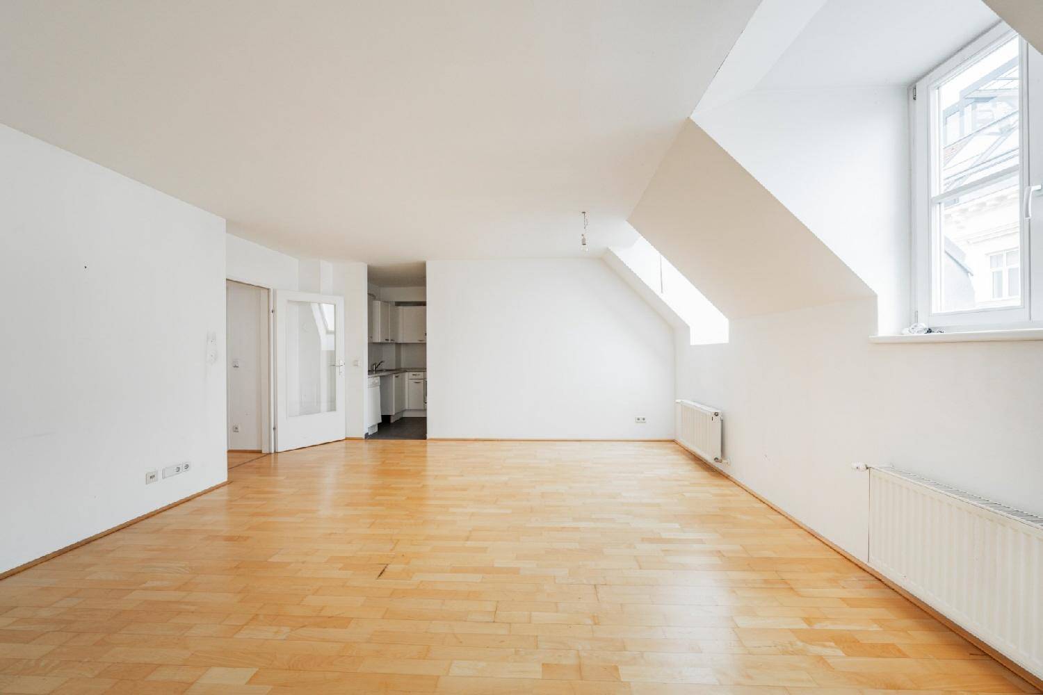 Heller Wohnbereich mit Holzfußboden und Dachschrägen, mit Zugang zu einer separaten Küche.