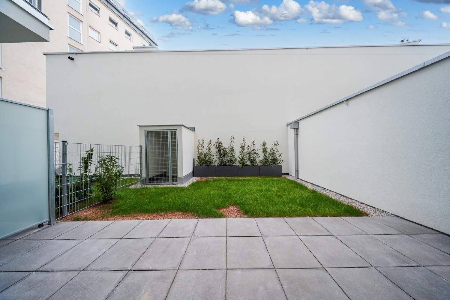 Blick auf den kleinen privaten Gartenbereich mit gepflasterter Terrasse, Rasen und einem Geräteschuppen.