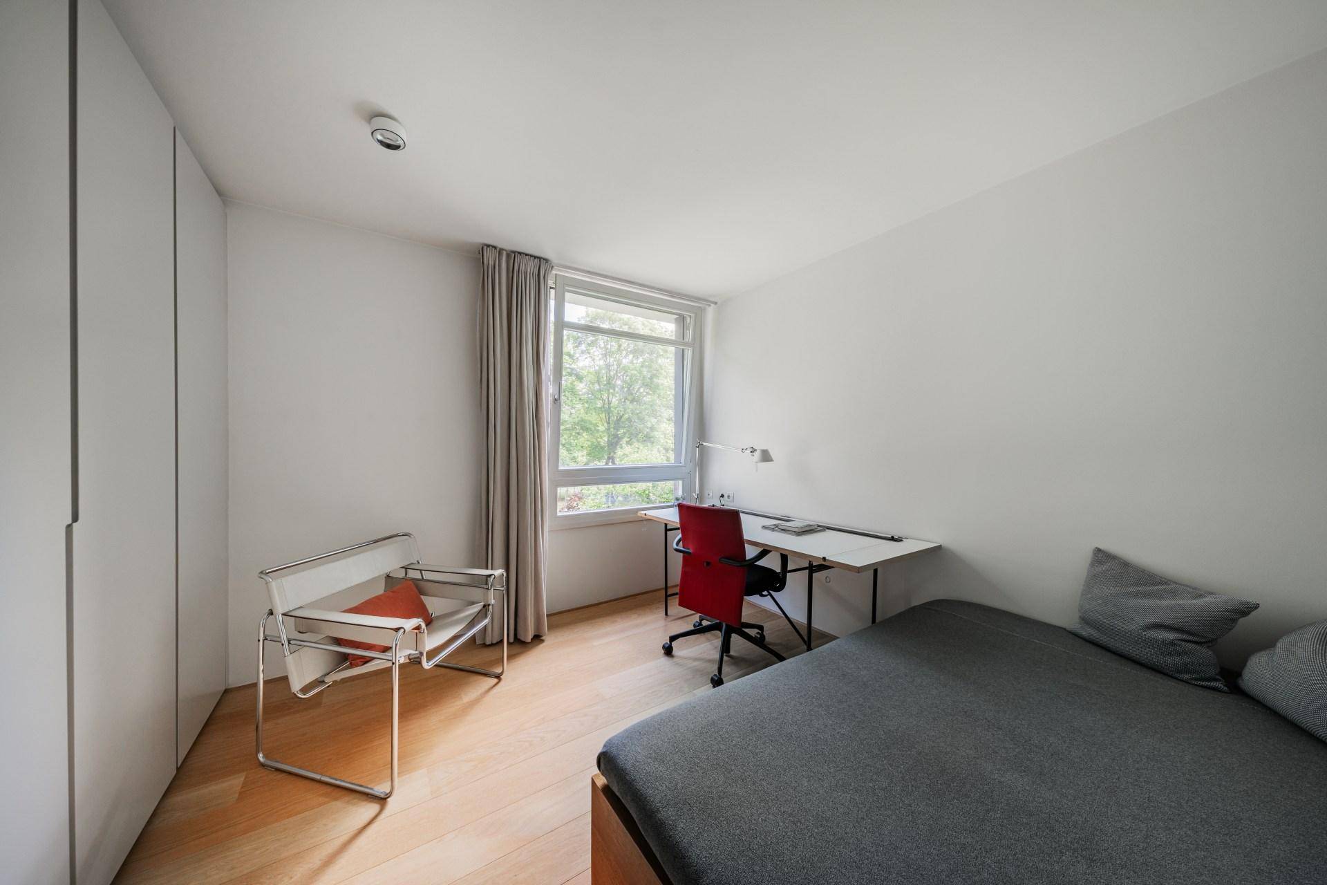Modernes Schlafzimmer mit Schreibtisch, Holzboden und viel Tageslicht.
