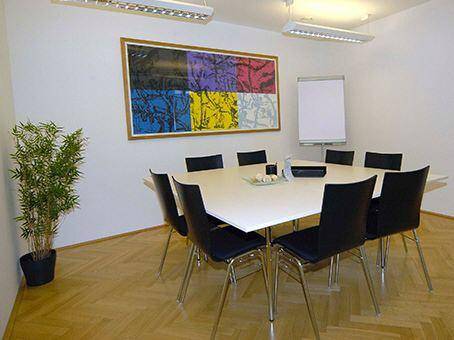Besprechungsraum mit quadratischem Tisch, schwarzen Stühlen und einem großen, farbenfrohen Kunstwerk an der Wand.