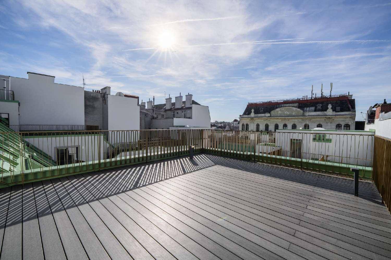 Geräumige Dachterrasse mit Holzboden und weitem Blick über die Stadt unter blauem Himmel.