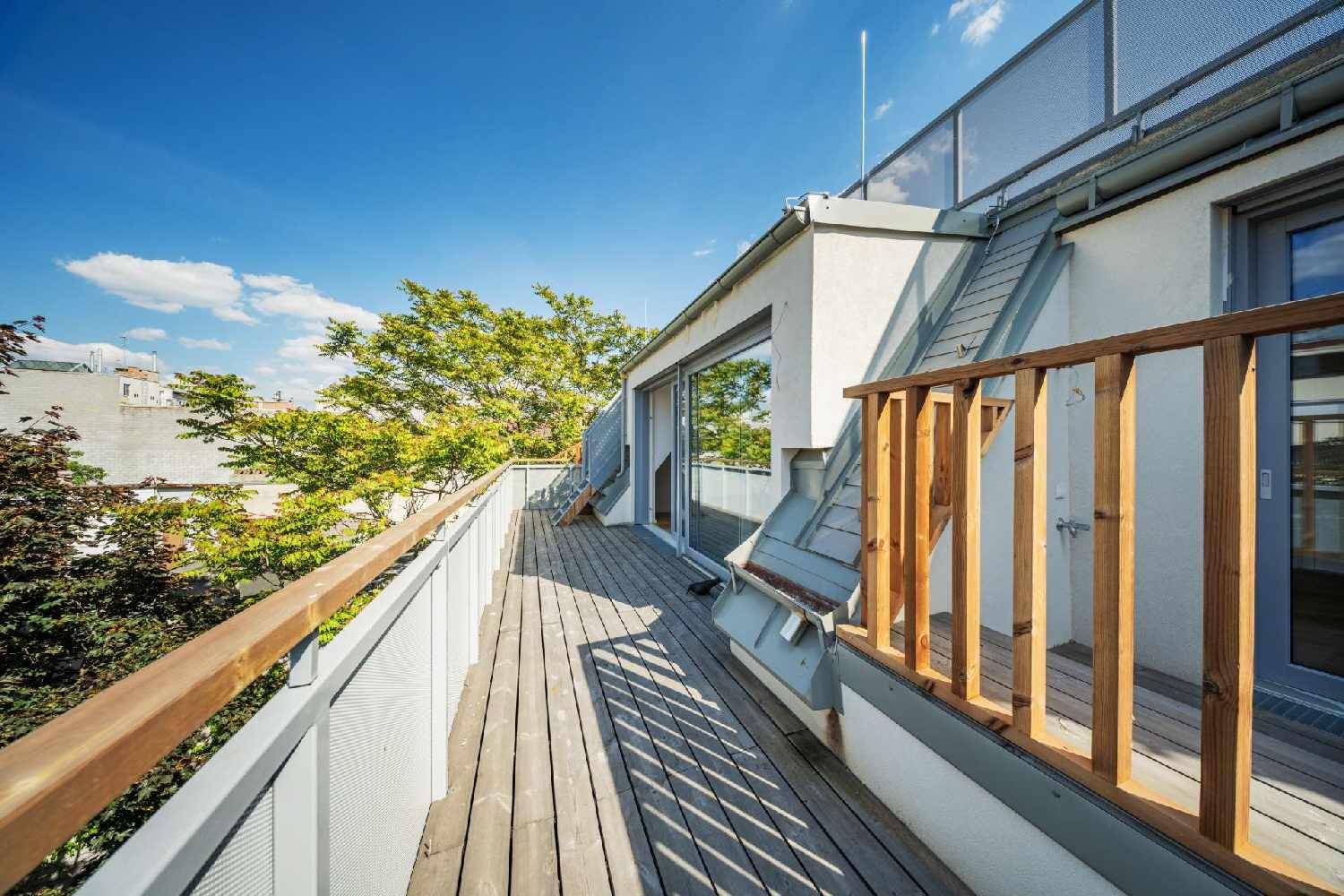 Langer Holzbalkon mit moderner Brüstung und Blick auf die umliegenden Gebäude und Bäume.