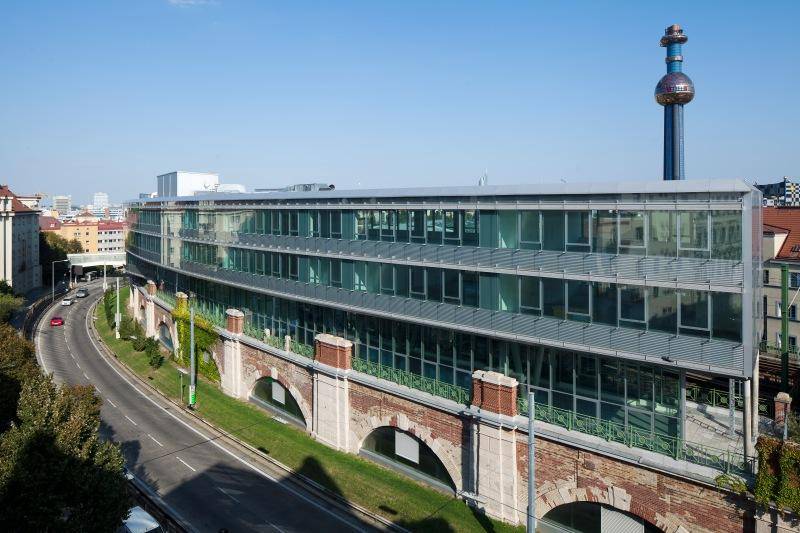 Bürogebäude mit moderner Glasfassade und historischem Mauerwerk im Vordergrund, eine gelungene Kombination.