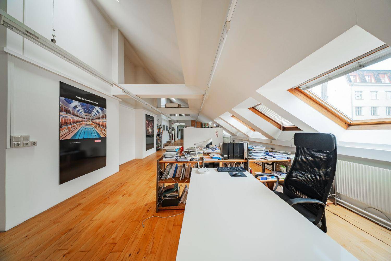 Helles und geräumiges Büro im Dachgeschoss mit Holzboden, sichtbaren Balken und mehreren Dachfenstern.