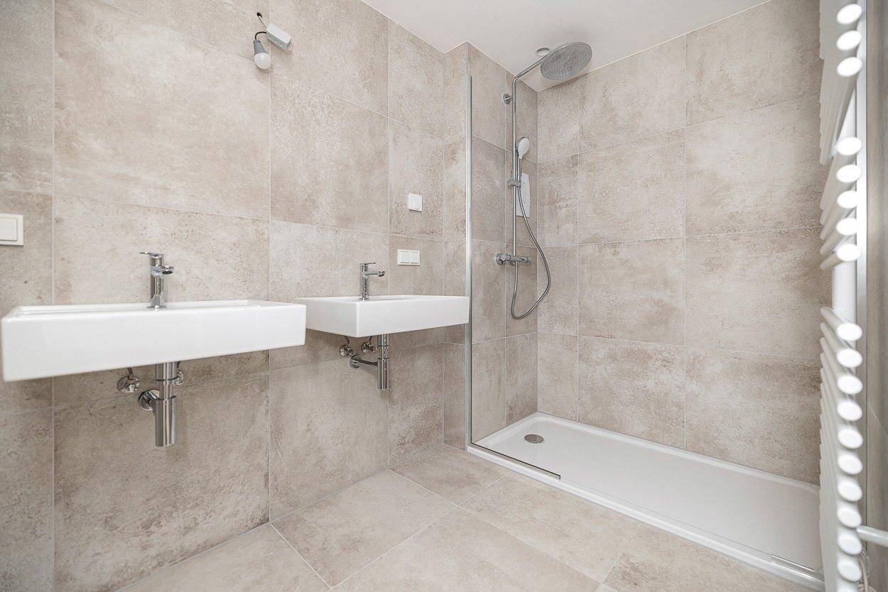 Modernes Badezimmer mit zwei Waschbecken, begehbarer Dusche und beigefarbenen Fliesen.