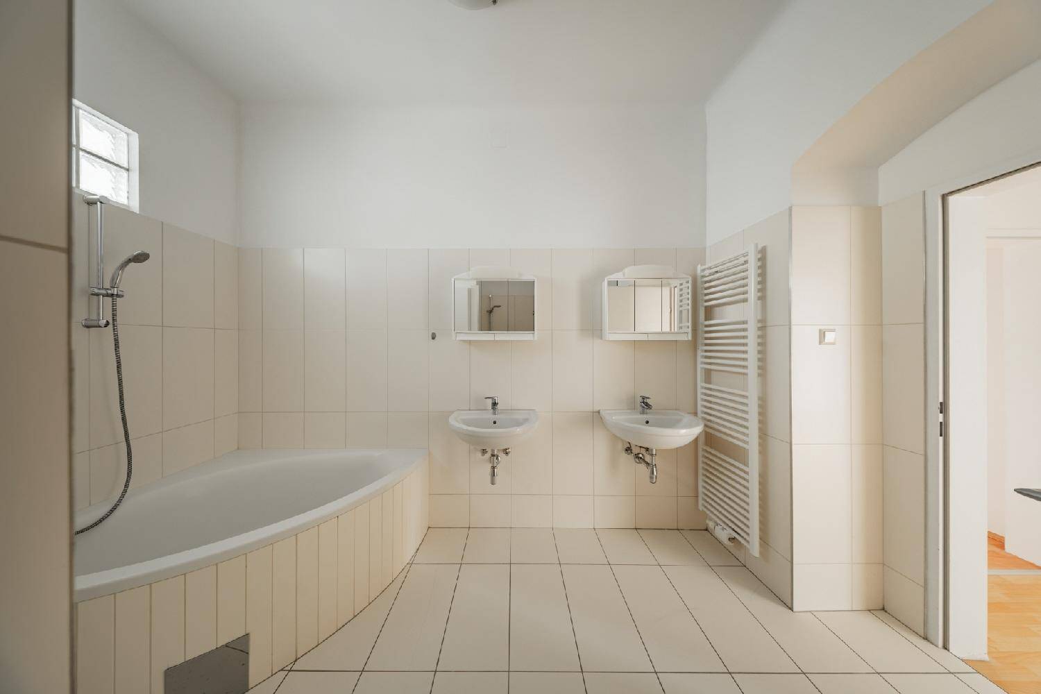 Geräumiges Badezimmer mit zwei Waschbecken, Badewanne und Handtuchheizkörper, hell gefliest.