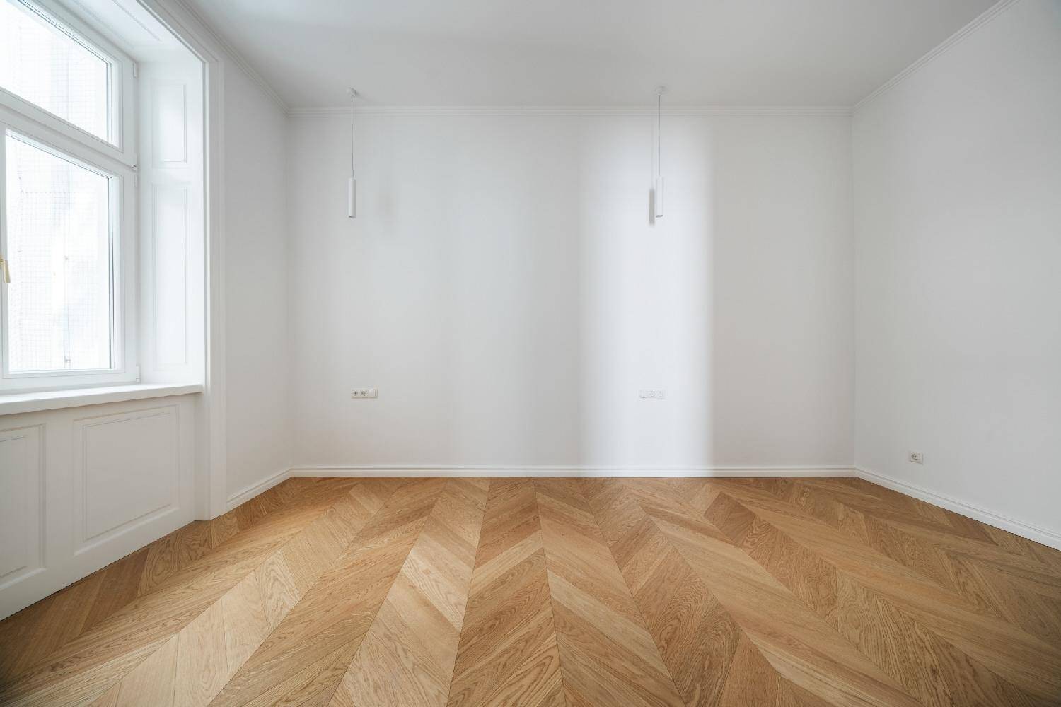 Ruhiges, helles Zimmer mit Fischgrätparkett, weißen Wänden und einem großen Fenster.