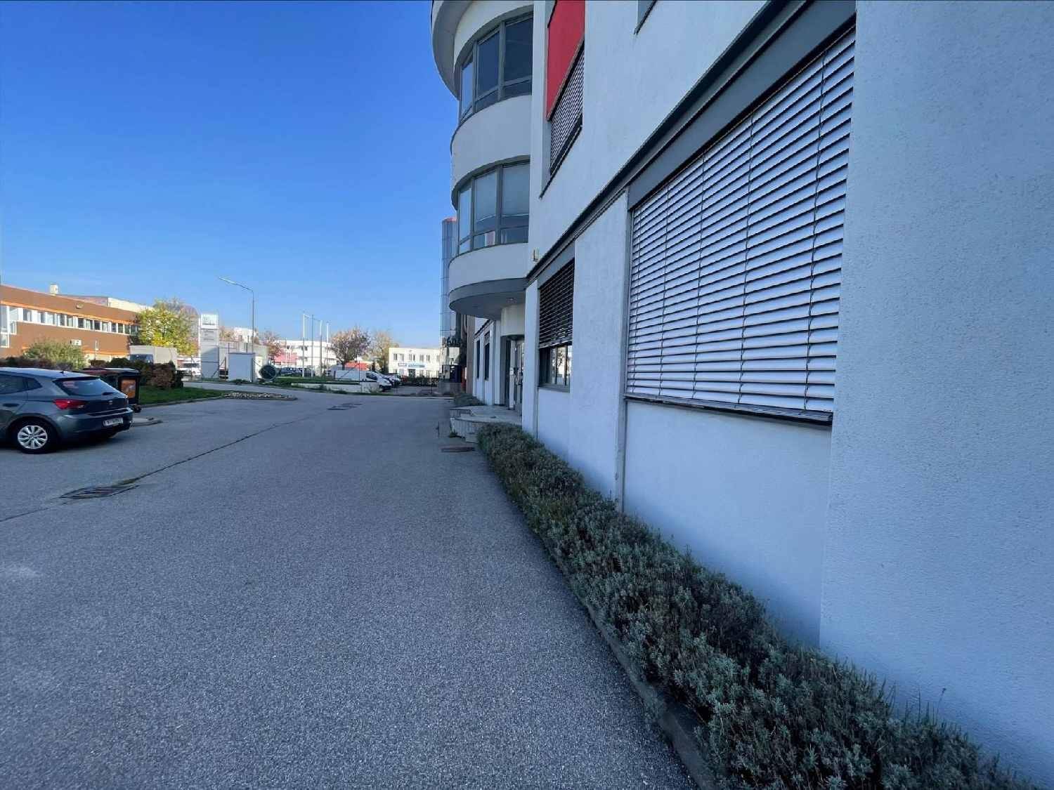 Moderne Gebäudefassade mit geschwungener Architektur, großen Fenstern und Rollläden.