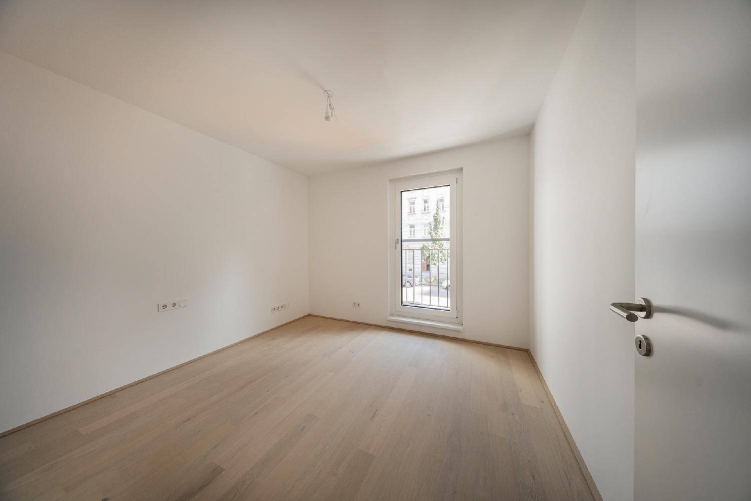 Helles Schlafzimmer mit Holzboden und französischem Balkon, ideal für individuelle Gestaltung.